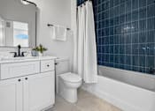 Thumbnail 25 of 36 - A white bathroom with a kitchen and shower combination with blue, textured tile. Along with modern finishes and toilet.