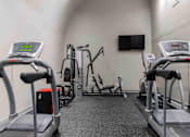 Thumbnail 44 of 66 - A gym with treadmills, elliptical machines, and a television.