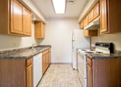 Thumbnail 10 of 24 - A kitchen with wooden cabinets and a white dishwasher at Hunters Run Apartments, Iowa, 50208