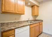 Thumbnail 7 of 24 - A kitchen with wooden cabinets and a granite countertop at Hunters Run Apartments, Newton, IA