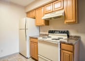 Thumbnail 8 of 24 - A kitchen with a white refrigerator, a white stove, and wooden cabinets at Hunters Run Apartments, Newton