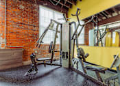 Thumbnail 21 of 25 - A gym with a red brick wall and a variety of exercise equipment at Spaulding Lofts Apartments, Grinnell, IA, 50112