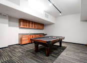 Thumbnail 35 of 50 - A pool table is in the middle of a room with a wooden cabinet and a pool cue on the right.