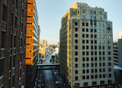 Thumbnail 49 of 50 - A city street with buildings on either side and a clear sky.