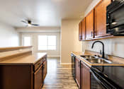 Thumbnail 33 of 56 - A kitchen with dark wood cabinets and a black stove top oven at Meadowlark Place Apartments, Iowa, 50111
