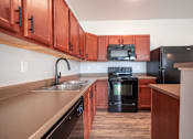 Thumbnail 7 of 56 - A kitchen with black appliances and wooden cabinets at Meadowlark Place Apartments, Grimes, Iowa