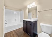 Thumbnail 9 of 47 - A bathroom with a toilet, counter space with black cabinets, and tub and shower combination at Melbourne Apartments in Des Moines, Iowa 50320.