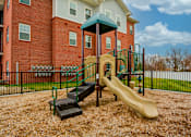Thumbnail 12 of 12 - A playground with a slide and steps in front of a red brick building.