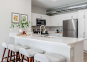 Thumbnail 36 of 69 - a kitchen with a large island with stools and a stainless steel refrigerator at Converge NW, Waukee Iowa  