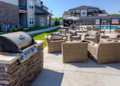 Thumbnail 31 of 50 - A barbecue grill is on a stone wall next to a patio with wicker chairs. at Stonegate Crossing Apartments, Clive, IA, 50325