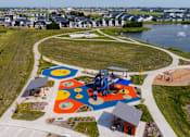 Thumbnail 44 of 57 - an aerial view of a playground in a park next to a lake at Rialto Townhomes Apartments, Iowa