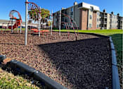Thumbnail 31 of 33 - A playground with a red swing set and a play structure in the background at Penbrooke Place Apartments, Sioux Falls, South Dakota