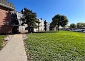 Thumbnail 32 of 33 - A grassy area in front of a building with a sidewalk at Penbrooke Place Apartments, South Dakota, 57106