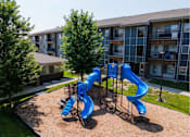 Thumbnail 19 of 35 - Playground with a blue slide in the foreground and apartment buildings in the background.