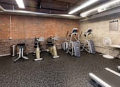 Thumbnail 10 of 13 - A gym with a brick wall and a variety of exercise equipment.at Riverpoint Lofts, Iowa, 50309
