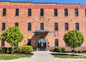 Thumbnail 11 of 13 - A red brick building with a large arched entrance and two trees in front.at Riverpoint Lofts, Des Moines, IA  