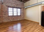 Thumbnail 2 of 13 - A room with wooden floors and a brick wall with a window.at Riverpoint Lofts, Des Moines, 50309  