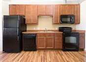 Thumbnail 5 of 13 - A black refrigerator, dishwasher, and oven in a kitchen with wooden cabinets.at Riverpoint Lofts, Des Moines, IA 50309  