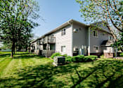 Thumbnail 7 of 10 - A house with a grey siding and a balcony is surrounded by green grass and trees at Peach Tree Apartments, Ankeny, IA