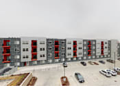 Thumbnail 31 of 31 - A large grey building with red accents and a parking lot in front at Vue Apartments, Des Moines