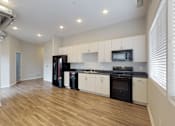 Thumbnail 17 of 31 - a kitchen with white cabinets and black appliances and a wooden floor at Vue Apartments, Des Moines