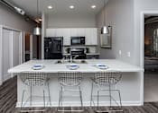 Thumbnail 5 of 31 - A modern kitchen with a white island and three chairs at Vue Apartments, Des Moines, IA