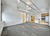 Thumbnail 21 of 50 - A room with a kitchen area in the background and a grey carpet in the foreground at The Des Moines Building Apartments, Iowa