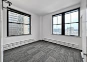 Thumbnail 15 of 50 - A room with a grey carpet and two windows overlooking a cityscape at The Des Moines Building Apartments, Des Moines, Iowa