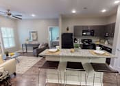 Thumbnail 7 of 32 - A kitchen with a black fridge and microwave, a dining table with chairs, and a living room with a couch and a coffee table. at The Barclay Apartments, IOWA, 50009