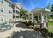 Thumbnail 16 of 22 - A gazebo is surrounded by a building and a patio with chairs.at Cornerstone Commons, Johnston, IA 50131  