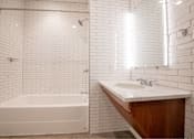 Thumbnail 12 of 39 - White tiled bathroom with a white bathtub, sink, and a white shower head at Clemens Building, Des Moines, 50309
