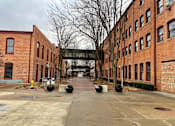 Thumbnail 99 of 99 - A long brick building with a walkway in front.at Plant 1 Lofts, N. Newton, IA  
