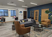 Thumbnail 5 of 7 - A living room with a grey couch, a brown chair, and a black coffee table.