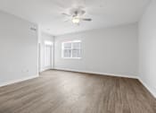Thumbnail 38 of 52 - A room with a ceiling fan and light, wooden flooring, and a window with a view of a building outside.