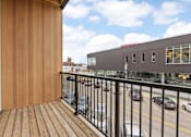 Thumbnail 20 of 52 - A balcony with a wooden floor and a black railing overlooking a street with cars.