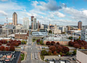 Thumbnail 32 of 37 - A cityscape with a mix of modern and older buildings, a parking lot, and trees with autumn foliage.