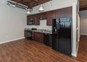 Thumbnail 4 of 25 - A black refrigerator is in a kitchen with wooden floors at Spaulding Lofts Apartments, Grinnell