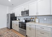 Thumbnail 11 of 77 - Galley kitchen with white cabinetry and corrugated backsplash at The Flats at West Glen Apartments, West Des Moines, IA