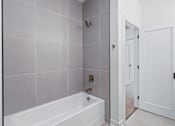 Thumbnail 71 of 77 - Modern bathroom with white tub and gray tile surround at The Flats at West Glen Apartments, West Des Moines, IA