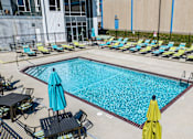 Thumbnail 23 of 40 - a swimming pool with lounge chairs and umbrellas near a building at Velocity Apartments, Des Moines, IA, 50309