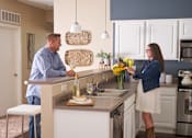Thumbnail 2 of 15 - a man and a woman standing at a kitchen island at The Winhall of Williams Pointe Apartments, Waukee