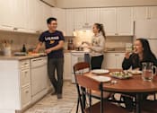 Thumbnail 17 of 17 - A man in a purple shirt is standing in a kitchen with a woman in a grey hoodie and another woman sitting at a table.