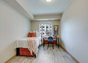 Thumbnail 26 of 33 - A bedroom with a bed, desk, and chair.
