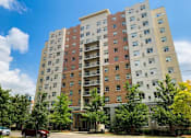 Thumbnail 3 of 17 - A tall apartment building with a red car parked in front.