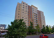 Thumbnail 4 of 17 - A red car is parked on the street in front of a tall apartment building.