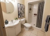 Thumbnail 12 of 17 - A bathroom with a white sink and toilet, a grey towel, and a mirror.