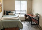 Thumbnail 15 of 17 - A bedroom with a bed, desk, and chair.