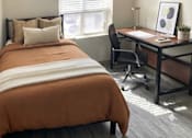 Thumbnail 13 of 17 - A bedroom with a bed, desk, and chair.