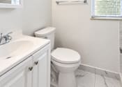Thumbnail 10 of 19 - A white bathroom with a toilet, sink, and a window with blinds.