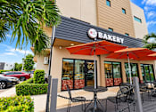 Thumbnail 2 of 48 - A bakery with a red umbrella and chairs outside.